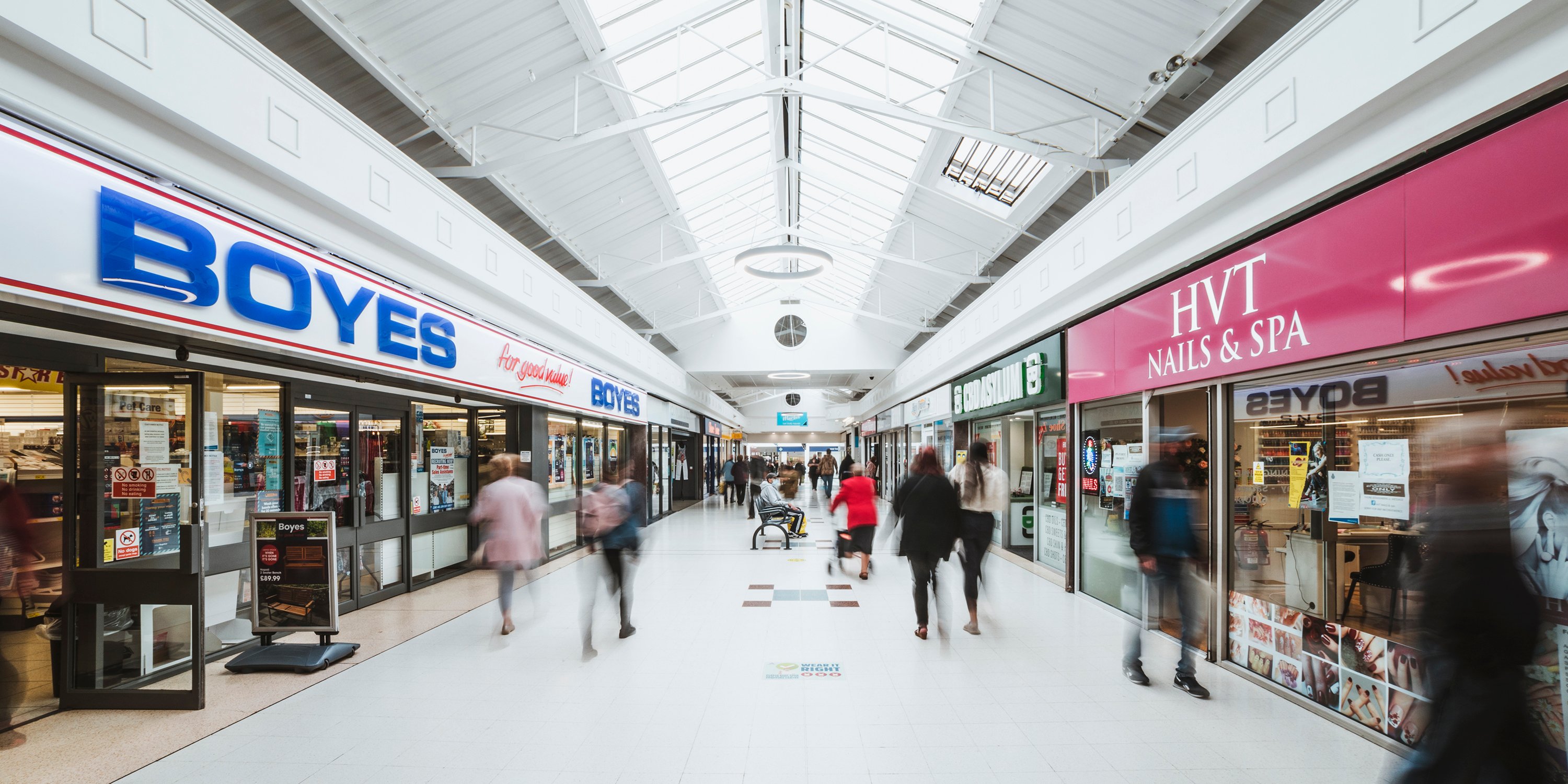 Interior of North Point Shopping Centre with Boyes on the left and HVT Nails & Spa on the right  with blurred shoppers in the middle